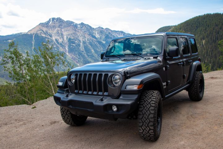 A black Jeep is parked on a forest road in the Colorado wilderness with a large mountain in the background