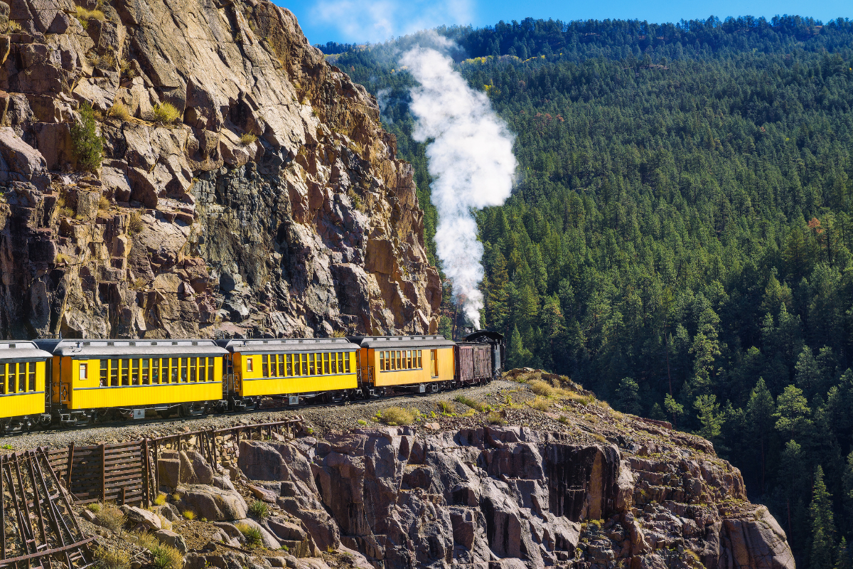 a train on a track with smoke coming out of a rocky mountain