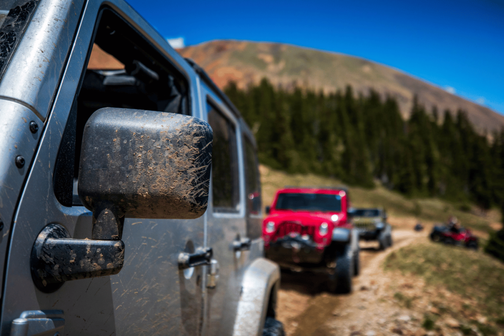 several jeeps drive on a trail in the mountains